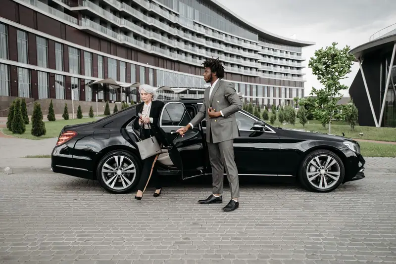 A chauffeur opens the door as a passenger steps out of a black Mercedes-Benz S-Class