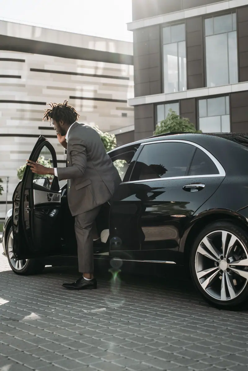 A passenger in a suit steps into the back of a black Mercedes-Benz S-Class